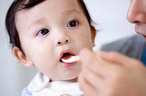 Em bé đang uống thuốc với sự hỗ trợ của người lớn, gợi nhắc tầm quan trọng của việc dùng thuốc đúng cách